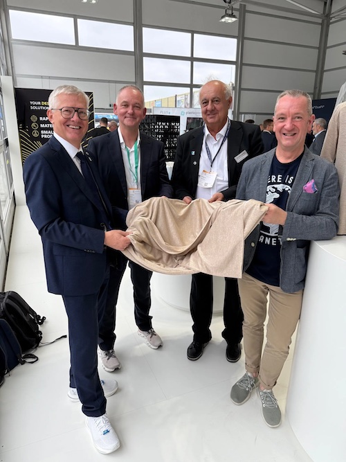 The same representatives  holding the new fabric made from 100% recycled polyester at the Edvanced Recycling Center, where EREMA demonstrates live recycling and products made of recyclate during the K show. © 2025 EREMA